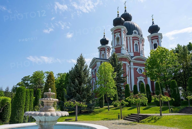 Orthodox church with red and white accents surrounded by a well-kept garden with a fountain, blue sky in the background, Cathedral of the Nativity of the Virgin Mary, Curchi monastery, Orhei district, Republic of Moldova, Moldova