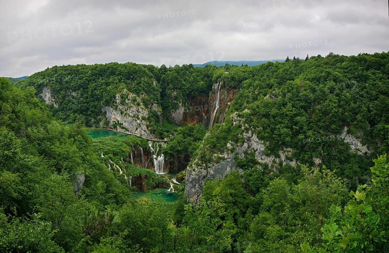 Panoramic view of a waterfall surrounded by thick green forest and rivers under a cloudy sky, Plitvice Lakes National Park, Croatia