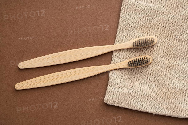 Top view of two bamboo toothbrushes on a brown surface, accompanied by natural beige fabric, emphasizing eco-friendly and sustainable toiletries