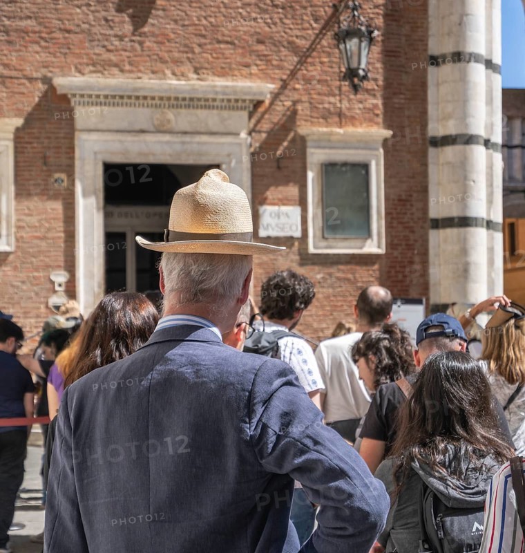 Tourist with too small head covering, summer hat with brim, Siena, Tuscany, Italy