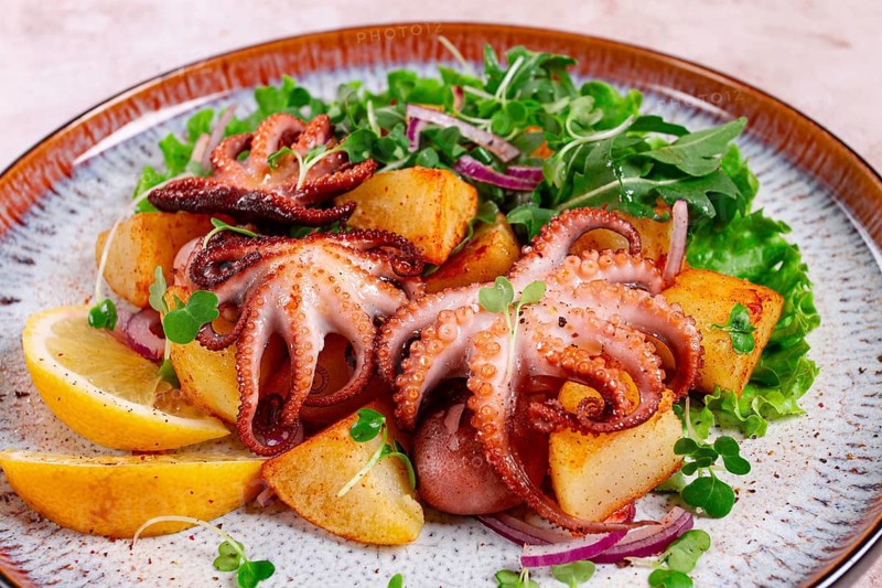 Grilled octopus with baked potatoes and fresh herbs, on a decorative plate, homemade