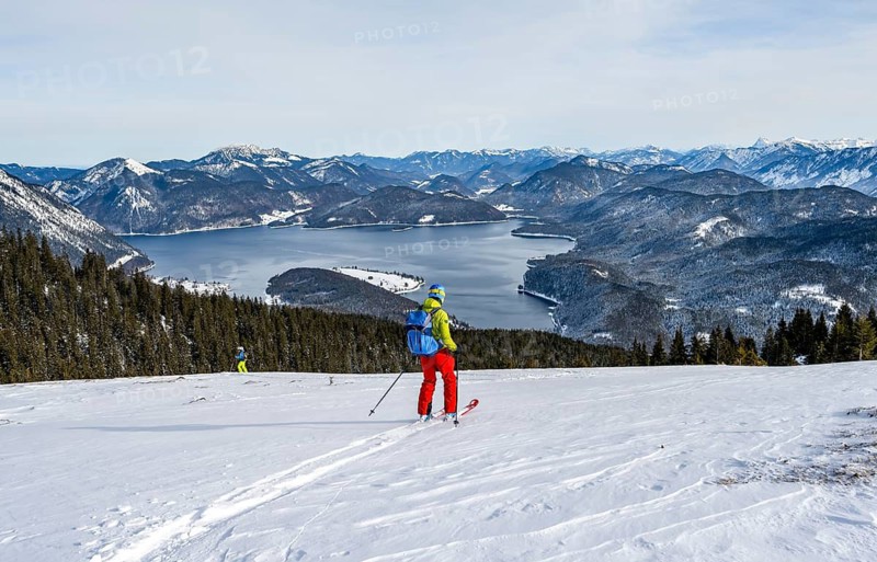 Skiers skiing down the Simetsberg, view of Walchensee and mountain panorama, Estergebirge, Bavarian Prealps, Bavaria Germany