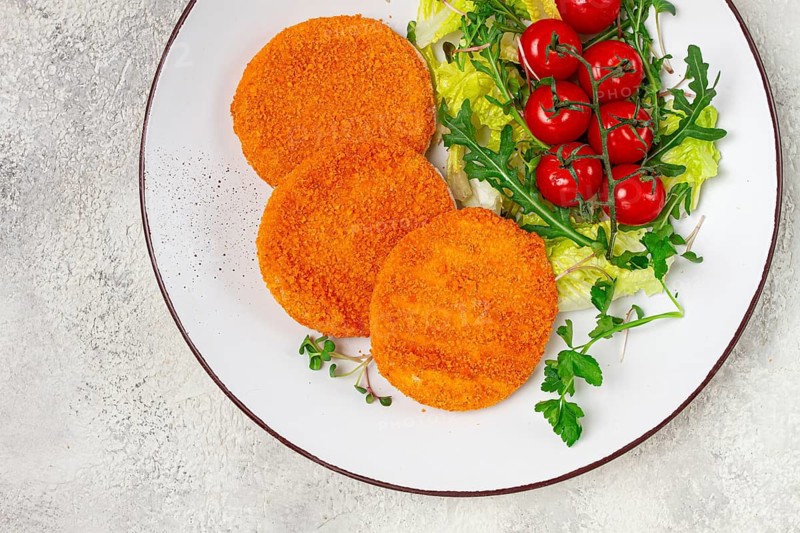 Crispy fried fish cutlets, fish burgers, on a white plate, with fresh lettuce leaves, arugula and cherry tomatoes, homemade, no people