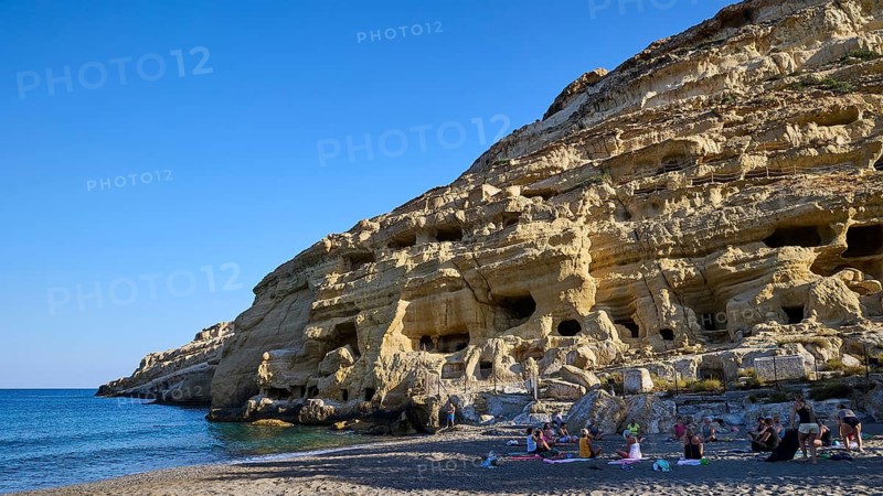 Neolithic caves, former hippie paradise, woman yoga group, people on the beach in front of impressive rock formations in clear skies, Matala, south coast, Crete, Greek islands, Greece