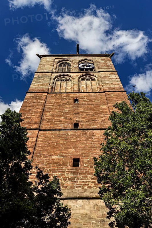 Historic brick tower with clock, surrounded by trees and under a blue sky with clouds, The tower of the town church in Bad Hersfeld