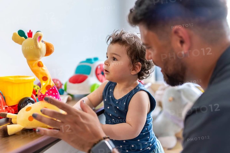 Father and baby son engaging in playful interaction at home, with the toddler happily reaching for a giraffe toy, highlighting family bonding, childhood development, and parental love