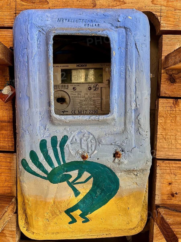 Decorated electricity meter with blue-yellow art and stylized dance motif on wooden wall, Matala, Neolithic caves, former hippie paradise, central south coast, Crete, Greek Islands, Greece