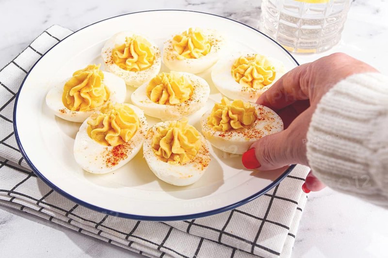 Stuffed eggs with paprika, on a plate, a woman's hand reaches for it