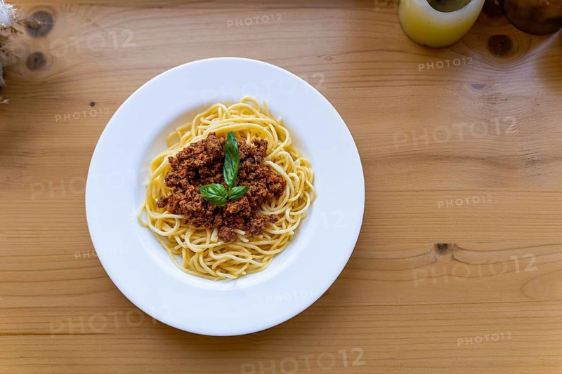 Spaghetti bolognese in a white plate, decorated with basil leaf on a wooden table, View from above. A classic dish of Italian cuisine