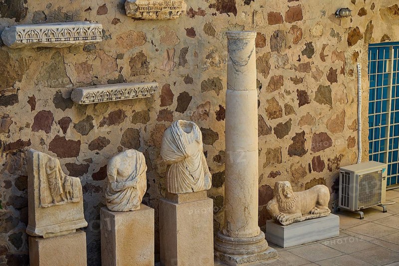 Plaka Archaeological Museum, ancient sculptures and a column in front of a stone wall in an archaeological site, Plaka, main town in Milos, island of Milos, volcanic island, Cyclades, Greek islands, Greece