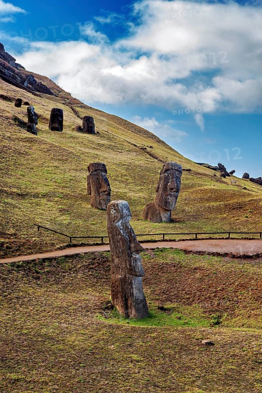 Several Moai statues on a green hill with a blue sky full of clouds, The Moai statues on Easter Island in the Pacific Ocean