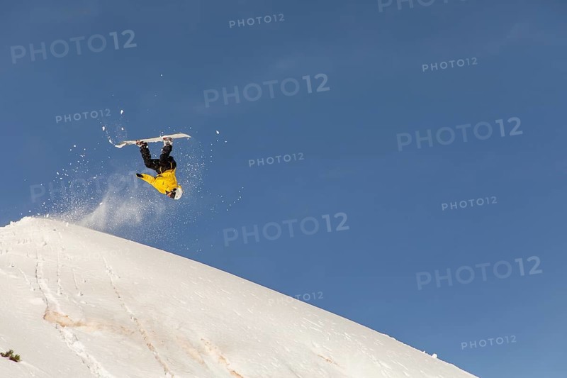 A snowboarder performs an exhilarating trick in the backcountry, surrounded by pristine powder and clear blue skies, showcasing the thrill of extreme winter sports in the mountains