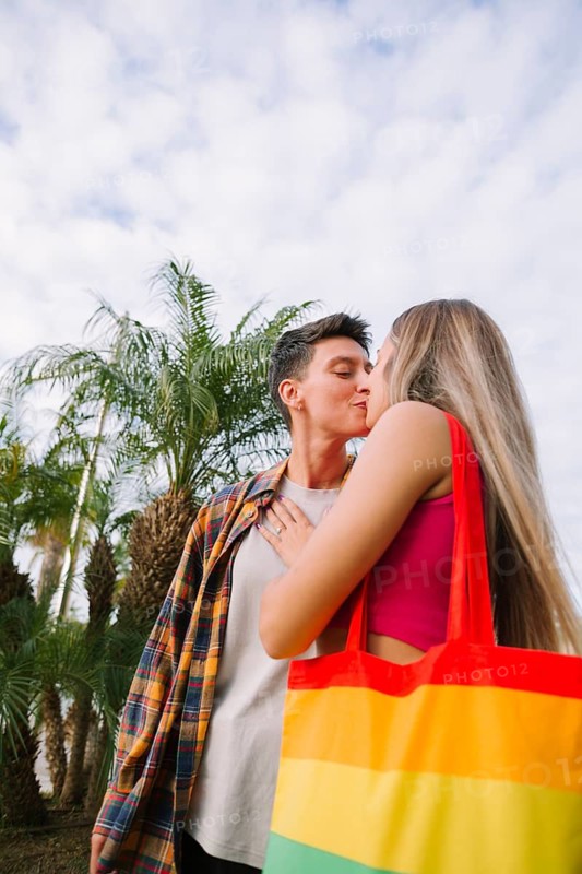 A lesbian couple shares a tender moment outdoors, exuding love and joy. With a rainbow bag as a symbol of pride, this image beautifully captures diversity and togetherness