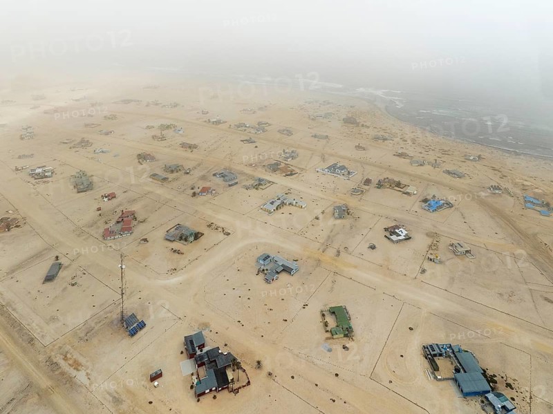 The odd holiday settlement of Wlotzkasbaken at the Atlantic coast often is shrouded in mist. Aerial view. Drone shot. Namib Desert, Skeleton Coast, Namibia