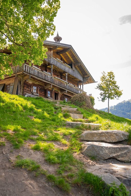 Wooden farmhouse with stone steps and green meadow, surrounded by trees and nature, Bergdoktor filming locations tour, Söll, Austria