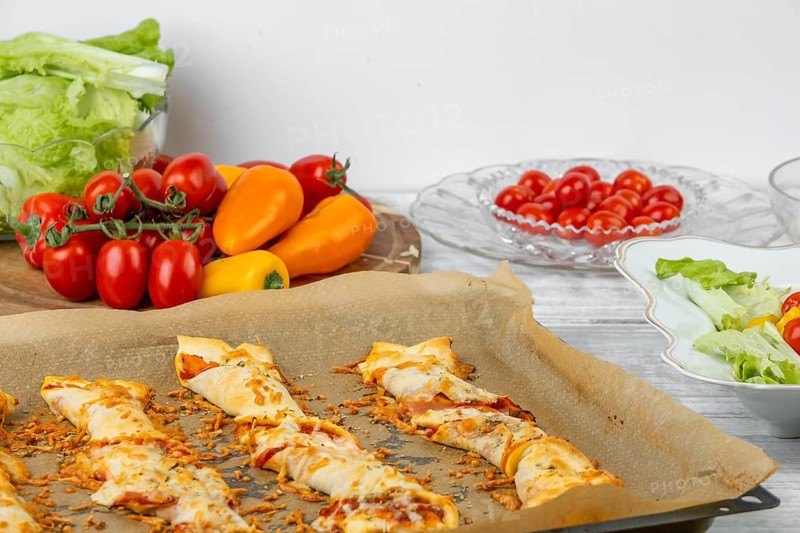 Baked pizza sticks on a tray, next to ingredients and fresh salad, pizza
