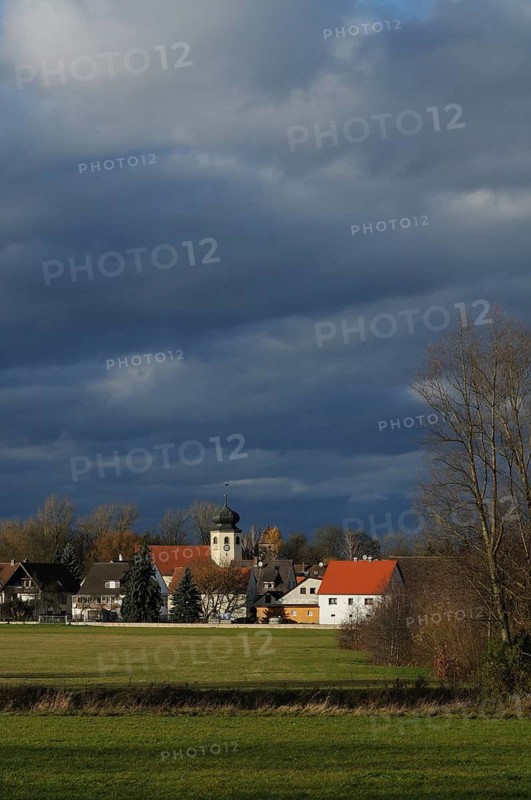 Small village with church under a dramatic sky, surrounded by meadows and bare trees in autumn, Muhr am See, Altmühlsee, Franconia