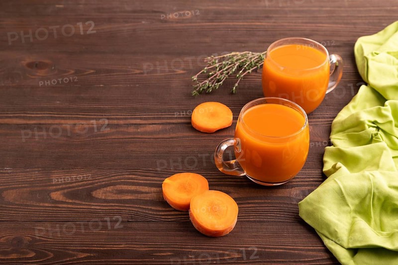 Two glasses with carrot juice, on wooden background and green textile. Diet, healthy eating concept. side view, copy space, minimalism