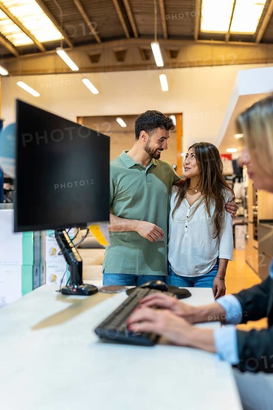 Young couple standing at a customer service desk in a home improvement store, consulting with an employee about renovation and interior design options for their new house