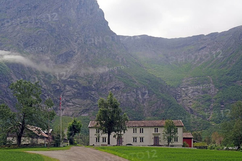 White house in a valley between high mountains with cloudy sky, Raumadalen, Trollvegen, Andalsnes, Norway