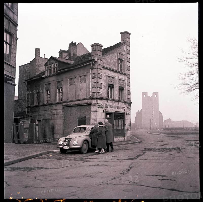 Magdeburg, post-war period, ruins of St. Catherine's church, demolished 1964-1966, vintage car, IFA F9, bleak, emptiness, black and white photo of an old building on a street corner with a parked car and people in front of it