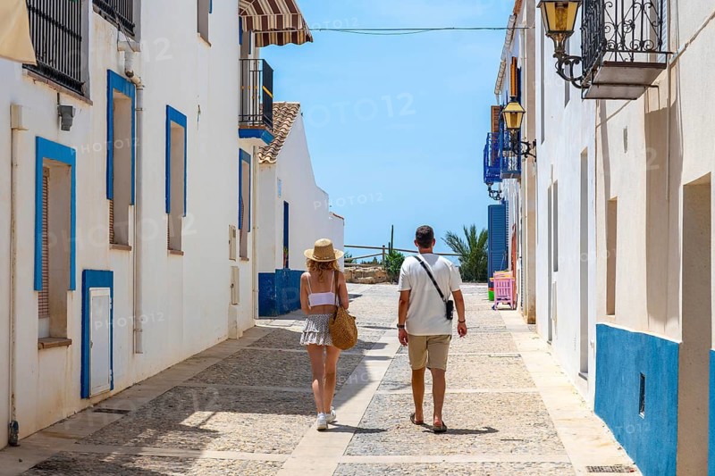 Couple enjoying a summer vacation, walking along a charming street with white houses and blue accents in tabarca island, spain, under a clear blue sky, experiencing mediterranean travel and tourism