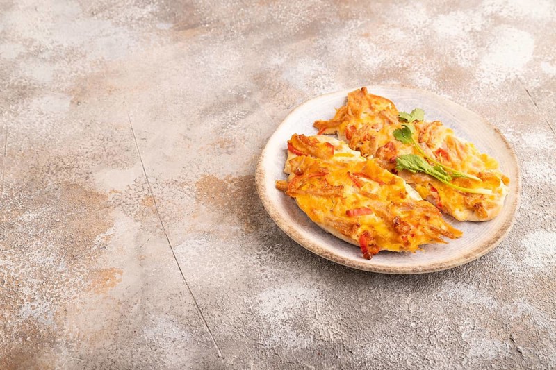 Baked chicken meat with cheese and tomatoes on brown concrete background. side view, copy space