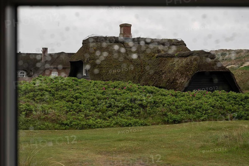 View through a window with blurred raindrops, traditional thatched Danish houses in the background, Houvig, North Sea, Denmark