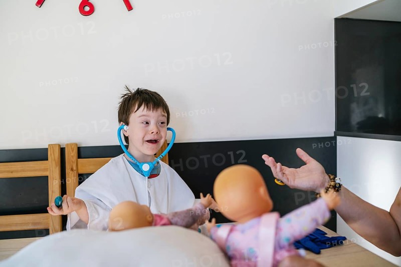 A young child with Down syndrome wearing a toy stethoscope, joyfully playing doctor with dolls. Their imaginative play highlights childhood development, creativity, and joyful learning