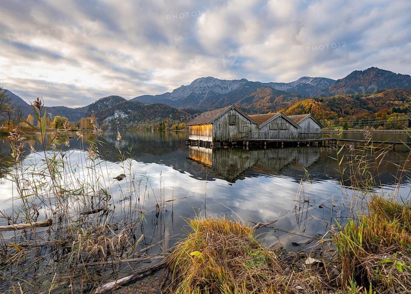 Boathouses in the lake at sunrise, Lake Kochel in autumn with reflection, behind mountain peaks Herzogstand and Heimgarten Upper Bavaria, Bavaria, Germany