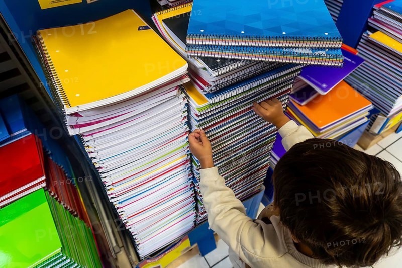 A child is reaching for a notebook on a shelf. The notebooks are stacked on top of each other, with some being yellow and others being blue. Back to school concept