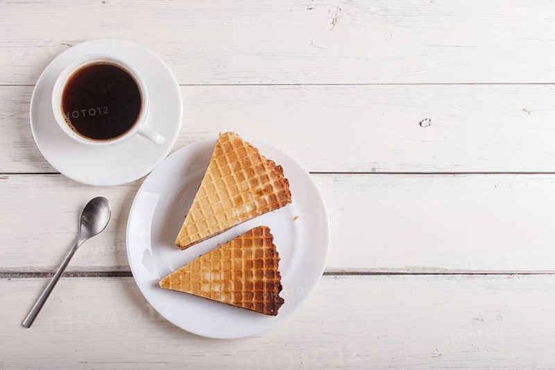 Waffle sandwiches with boiled condensed milk in plate on white wooden table with cup of coffee. closeup, copy space, top view