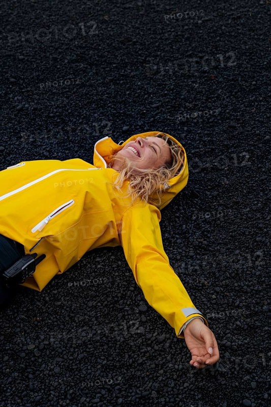 A woman in a yellow jacket enjoys a blissful moment lying on the black volcanic terrain of Timanfaya National Park, Lanzarote. The striking contrast highlights the natural beauty