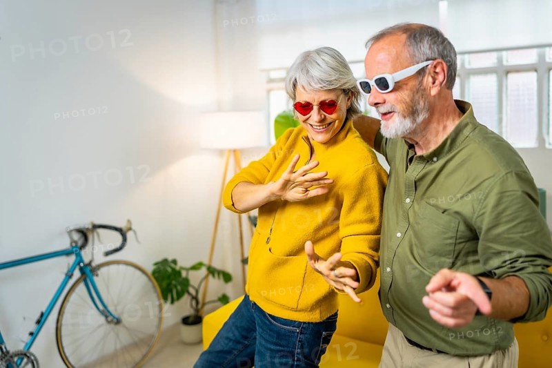 Happy modern senior couple with sunglasses dancing and having fun at home
