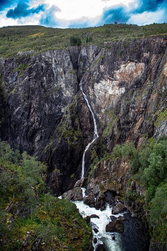 A high waterfall flows through rugged cliffs surrounded by thick vegetation, under a cloudy sky, The Vøringfossen Waterfall on the western edge of Hardangervidda, Norway, Scandinavia