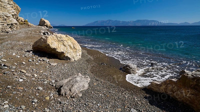 A quiet beach with pebbles and rocks, surrounded by crystal clear water and mountains in the distance, Empros Thermal Spa, Kos, Dodecanese, Greek Islands, Greece