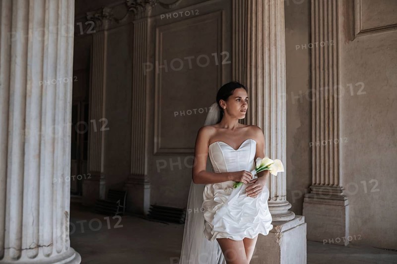 A bride in a white dress stands in an ancient villa in Treia, province of Macerata, Italy. The elegant architectural columns and serene atmosphere create a romantic setting