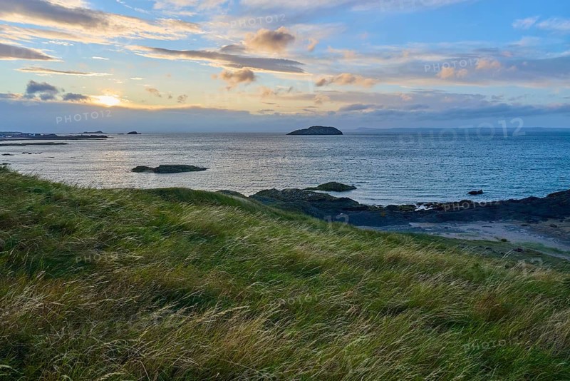 View of sea and island at sunset, with grassy hills in the foreground, North Berwick, East Lothian, Scotland, United Kingdom, Great Britain