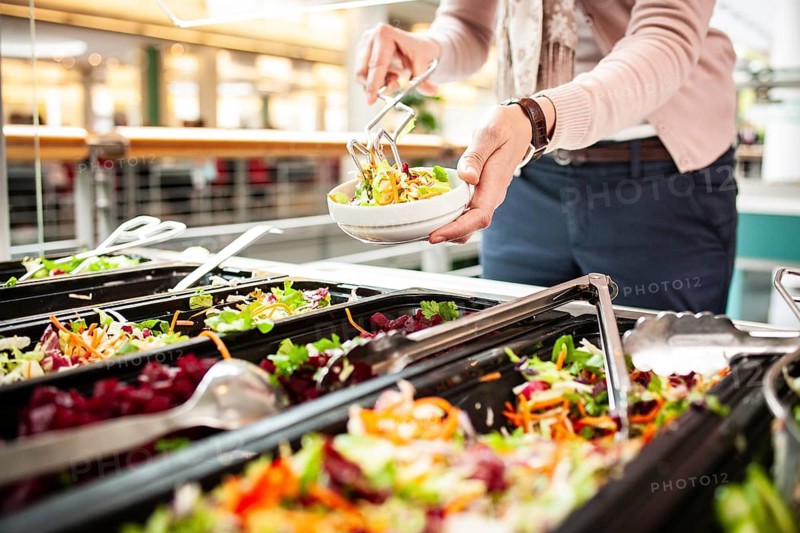 Fresh salads in a salad bar, a woman helps herself at the buffet