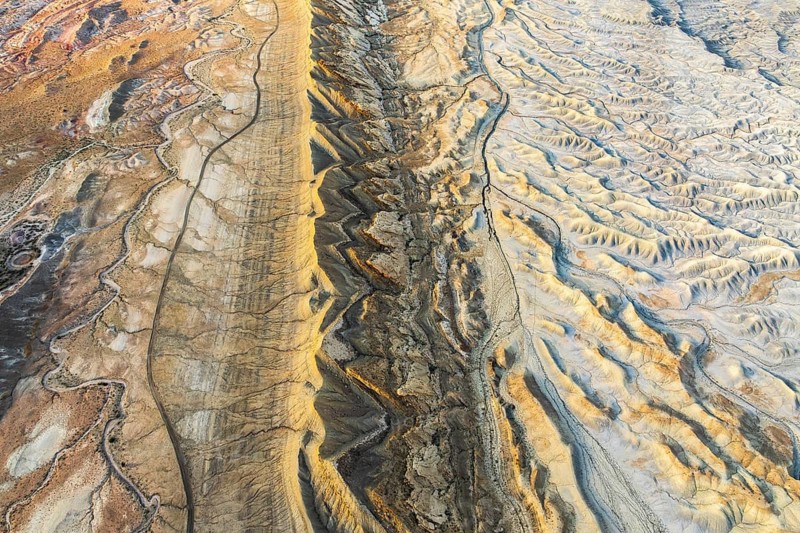 A stunning aerial view of Utah's golden sandstone desert highlights intricate geological patterns and textures, showcasing the region's natural beauty and unique formations