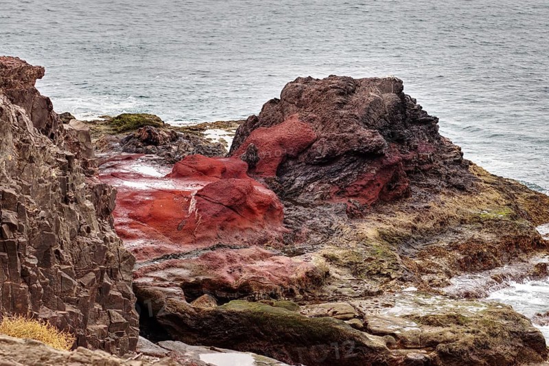 Red and black rocks jutting into the sea on a rugged coastline, Playa Blanca