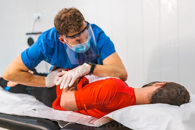 A physical therapist working on the hip of a patient. Physiotherapy with protective measures for the Coronavirus pandemic, COVID-19. Osteopathy, therapeutic chiromassage