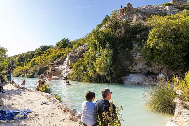 Bathers in one of the thermal pools between the cascades in the limestone on the steep slope of the Orcia Valley in the Parco dei Mulini, the mill park, which is fed with warm water from the thermal spring and was once used to power several horizontal wheel water mills, Bagno Vignoni, San Quirico d'Orcia, Province of Siena, Tuscany, Italy