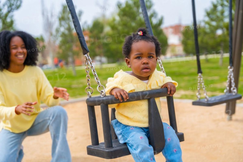 Smiling african mother pushing the swing of her daughter in the park