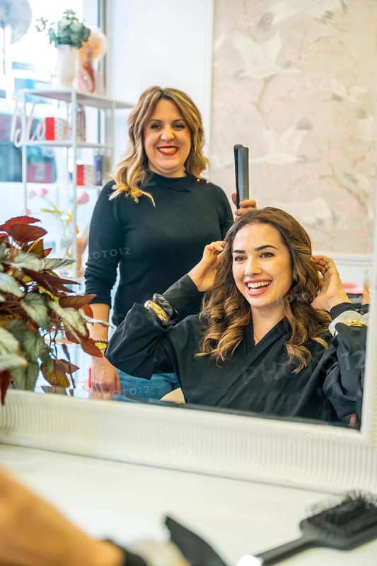 Happy young woman smiling as a professional hairdresser styles her curly brunette hair in a bright, modern beauty salon, enjoying pampering, confidence and transformation