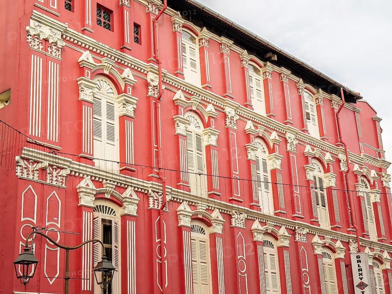 Intricate architectural details of a heritage building with a striking red facade, located in Singapore. The building showcases traditional colonial era design with ornate window frames and decorative moldings