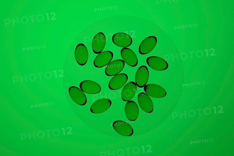 Transparent capsules filled with Omega-3 and Vitamin D oils scattered over a luminous green background, showcasing health and nutrition