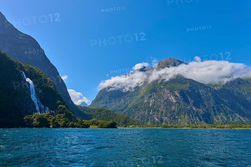 Blue fjord with waterfall in the background and impressive mountains under a blue sky, summer, Milford Sound, Te Anau, Fiordland National Park, South Island, New Zealand