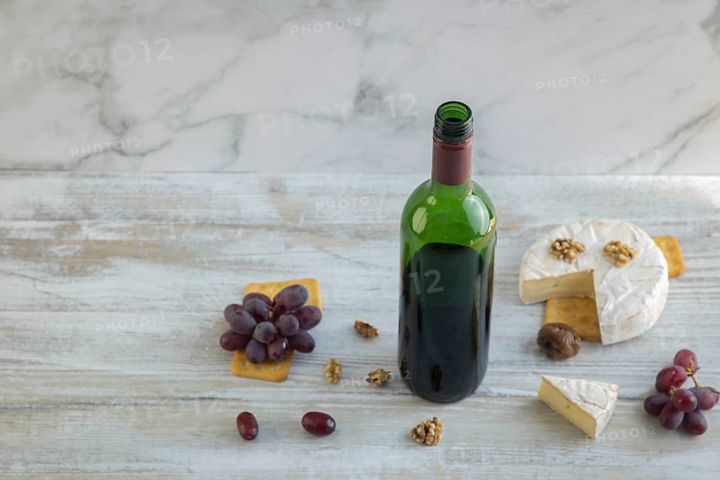 Wine bottle surrounded by camembert, grapes, nuts and crackers on a light-coloured background