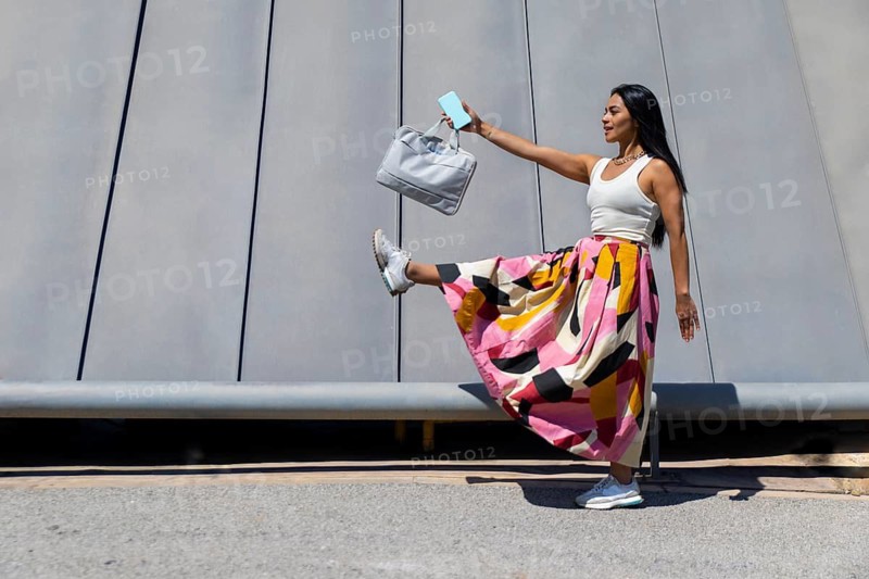 A stylish woman in a vibrant outfit contrasts against modern architecture. Captured mid-motion, she embodies the dynamic energy of urban life with elegance and flair